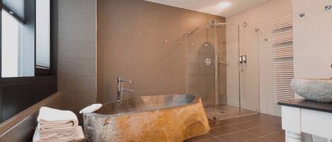 Un baño moderno con una bañera independiente, ducha con cerramiento de vidrio y tocador con lavabo de piedra.