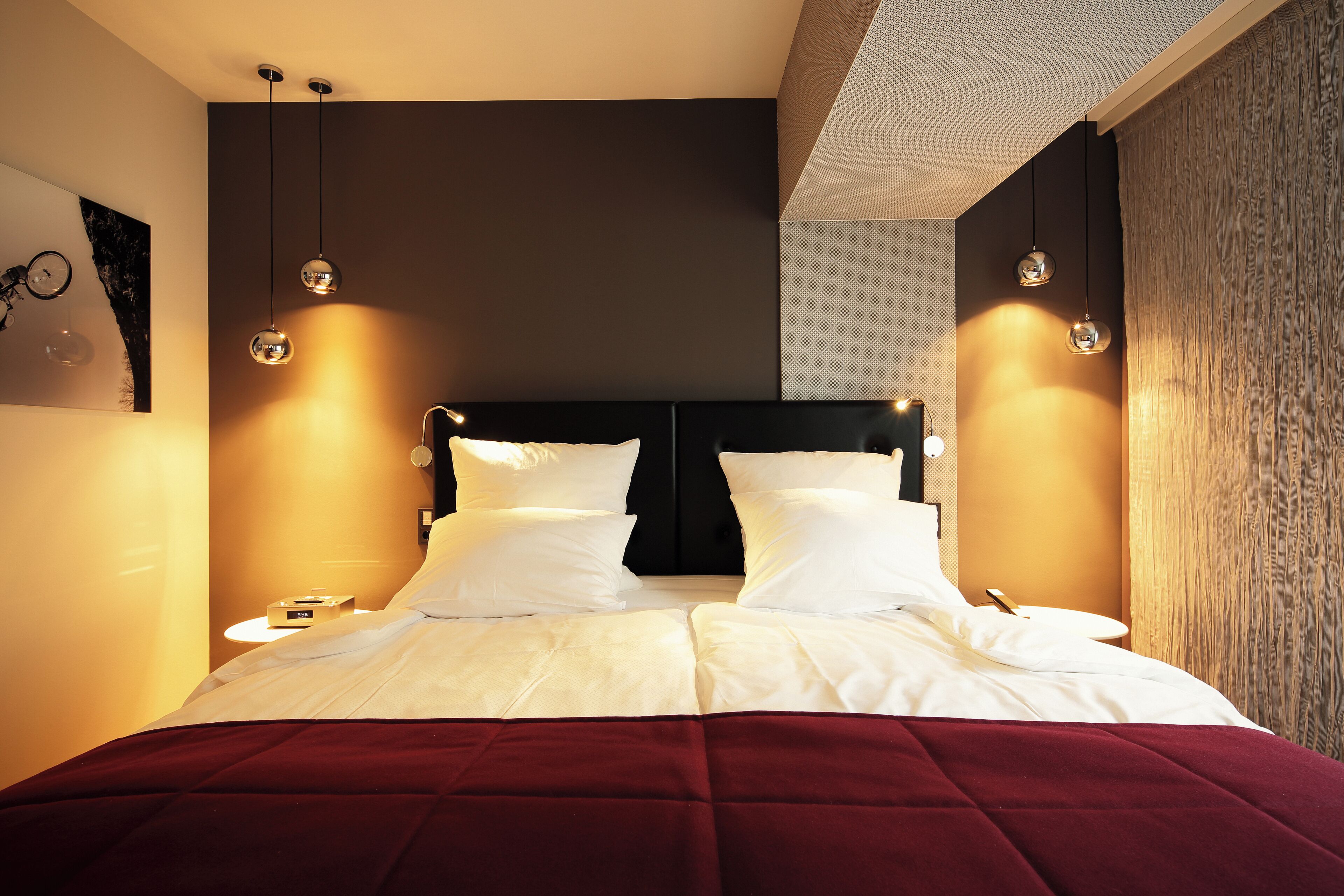 A modern hotel room with a large bed, two bedside tables, and pendant lighting.