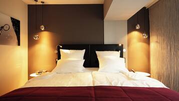 A modern hotel room with a large bed, two bedside tables, and pendant lighting.