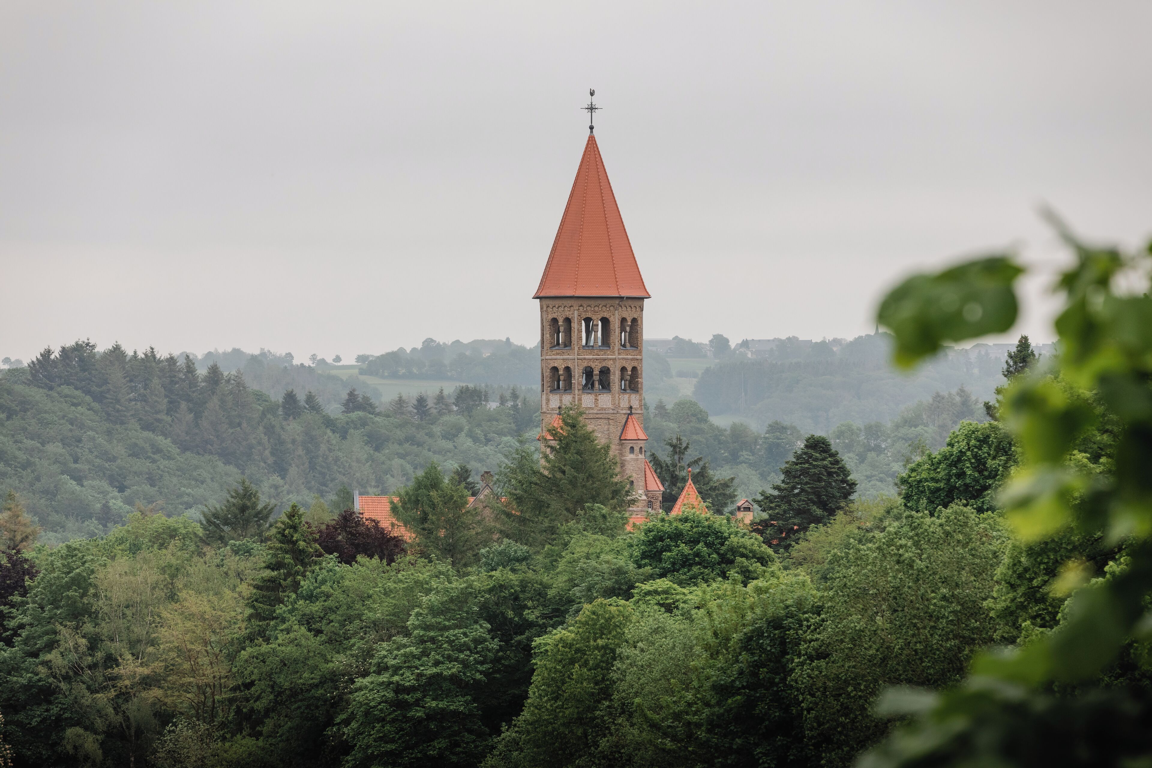 A tower with a red roof, surrounded by dense green trees.