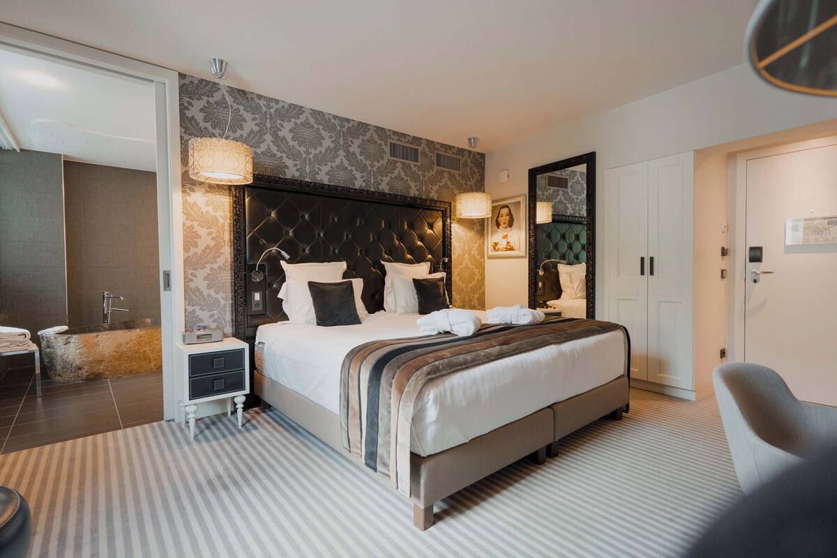 A modern hotel room with a large bed, a nightstand, a mirror, and a seating area.
