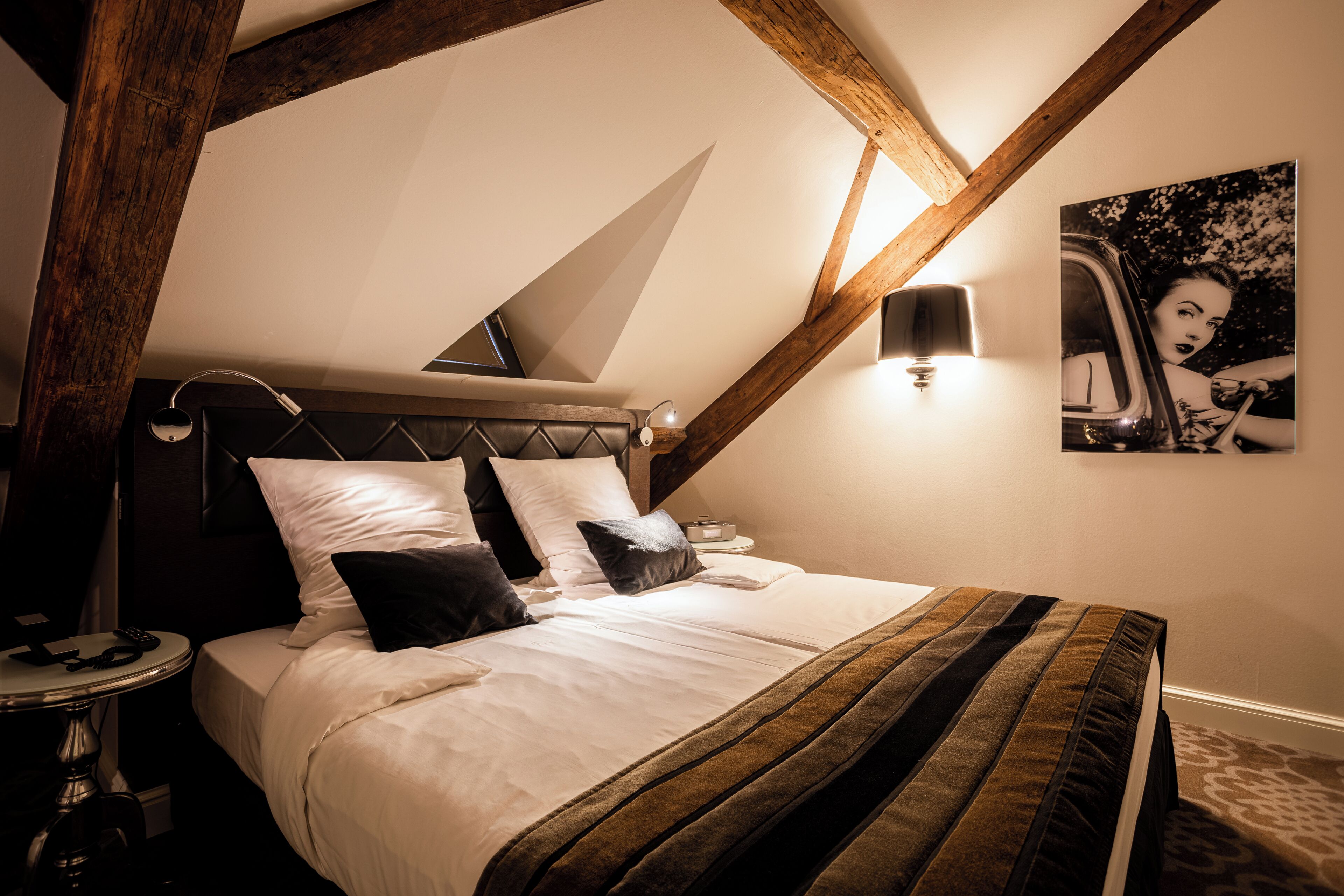 A bedroom with a bed, a nightstand, a lamp, and a painting on the wall.