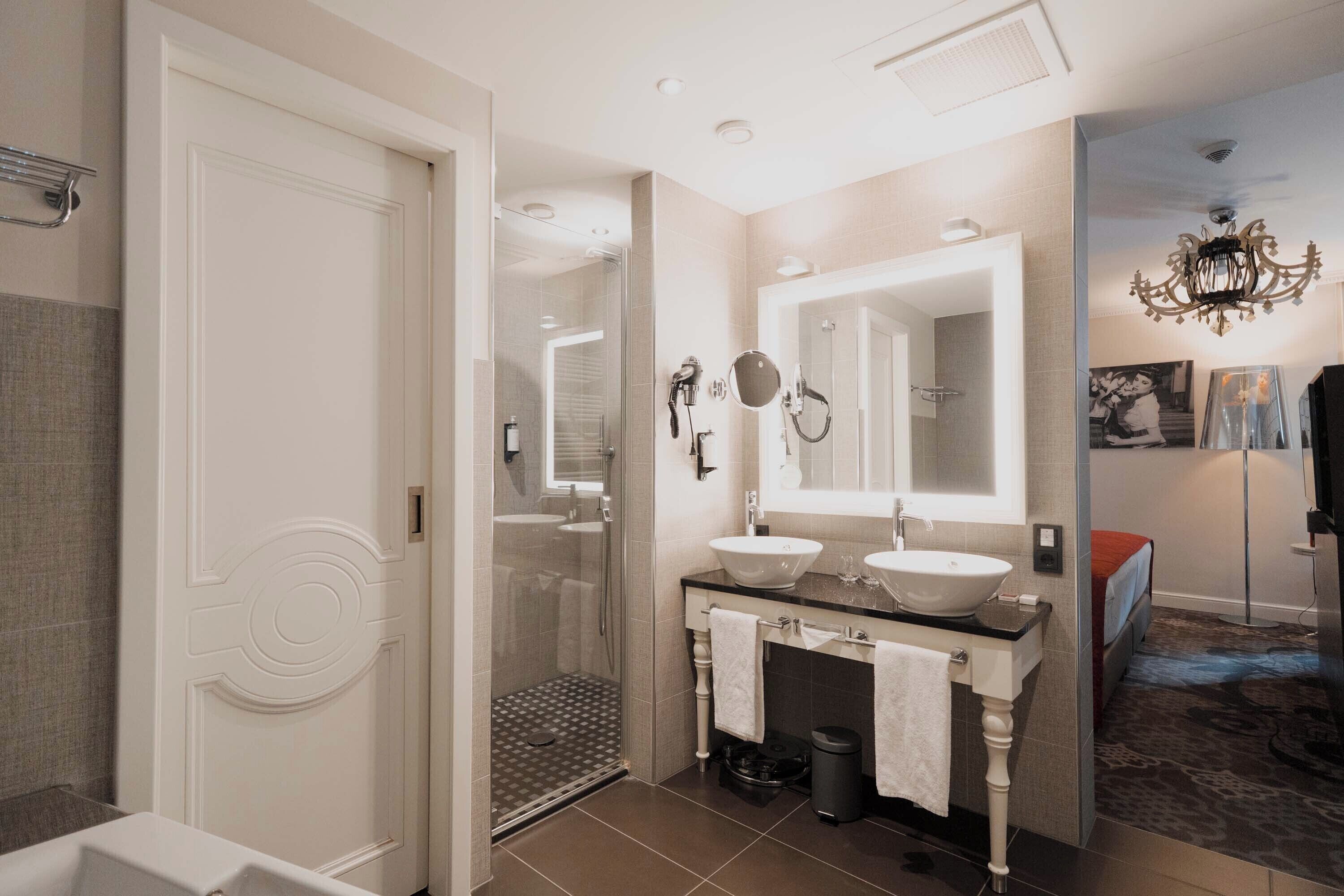 Un baño moderno con cabina de ducha, dos lavamanos y un espejo grande.
