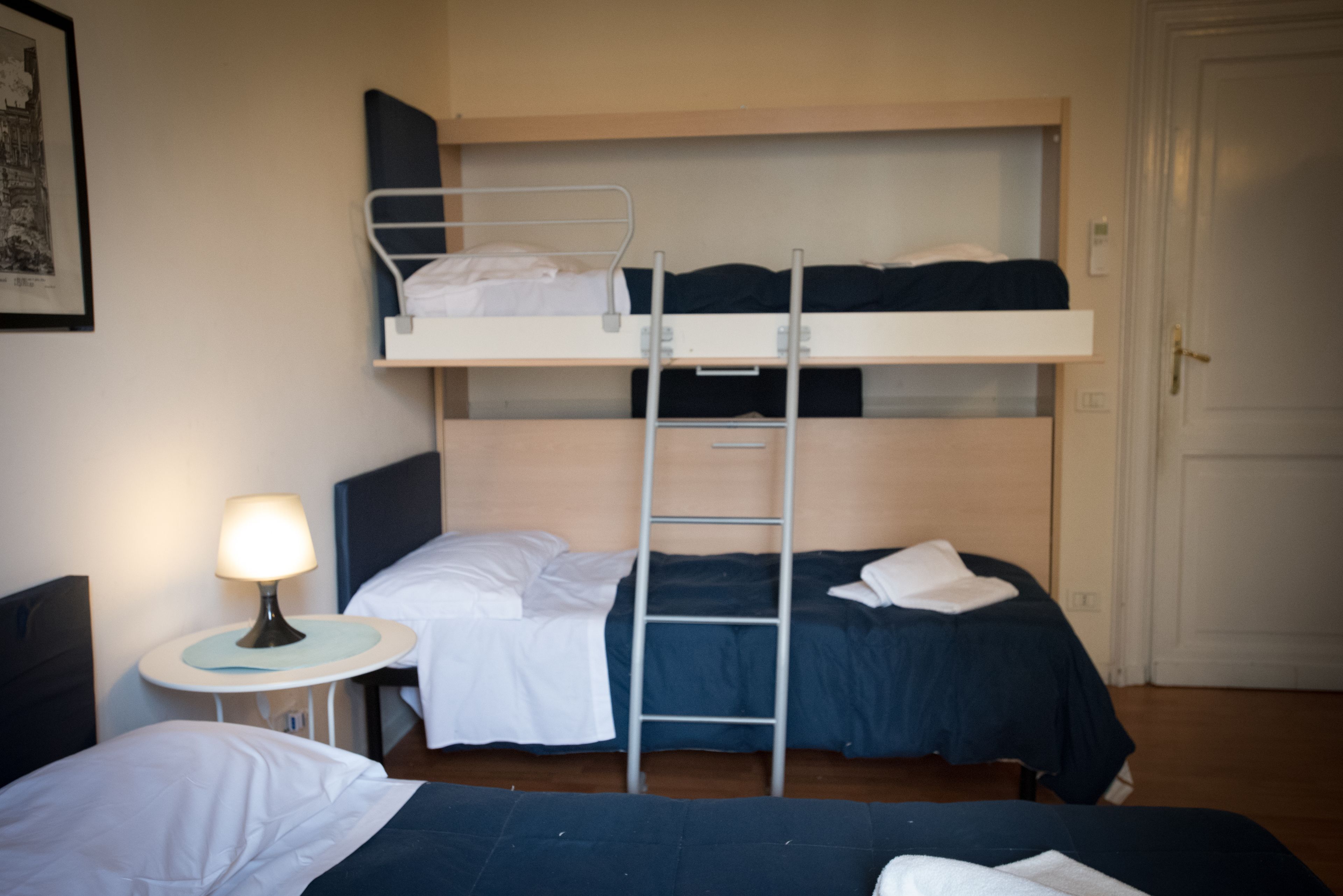 A bunk bed room with a ladder, a small table with a lamp, and a door.
