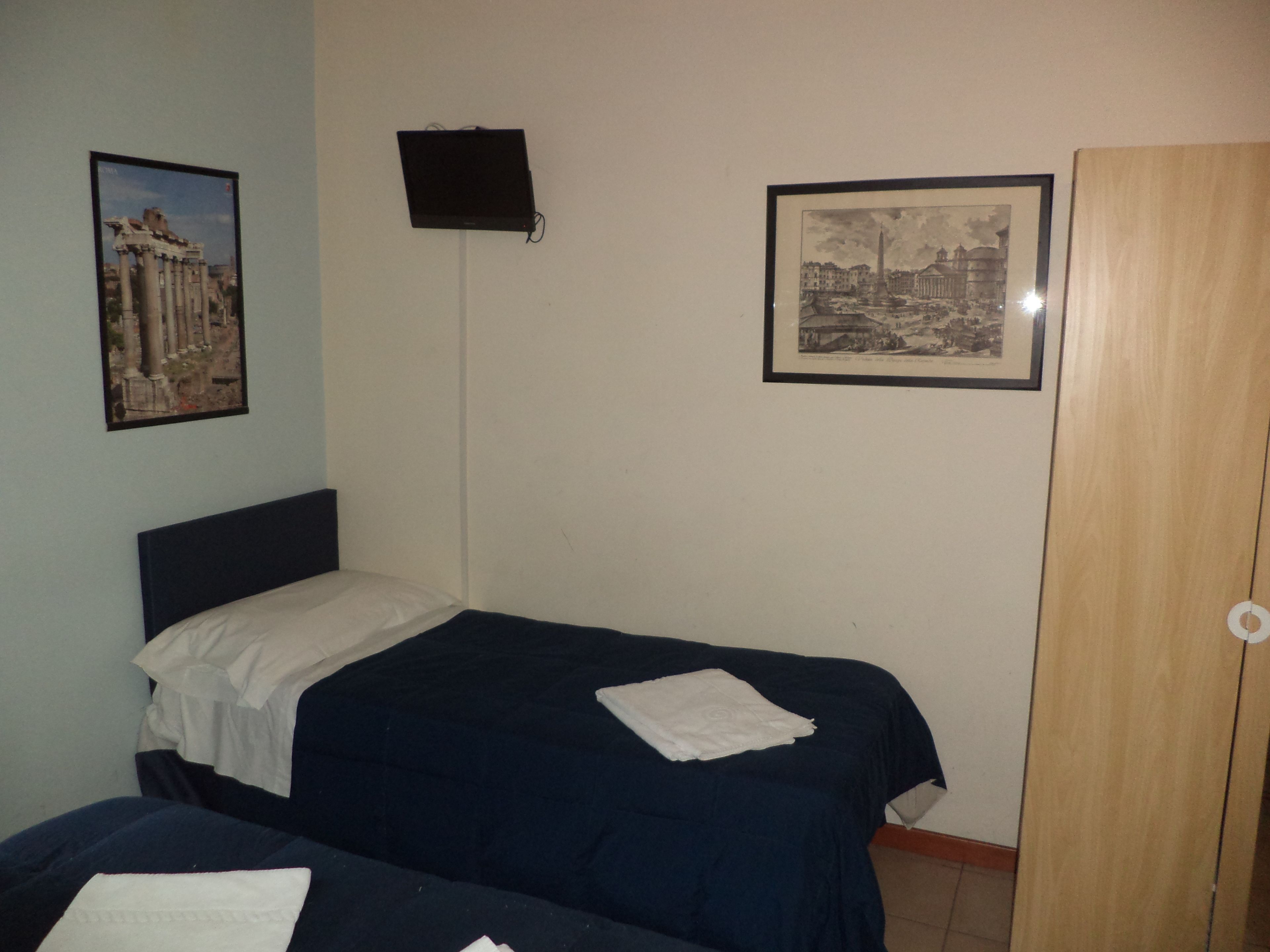 A bedroom with two beds, a wardrobe, and two framed pictures on the wall.