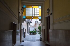 A narrow hallway with a tiled floor, potted plants, and a decorative stained glass window at the end. - Quo Vadis Roma 2 (Rome)