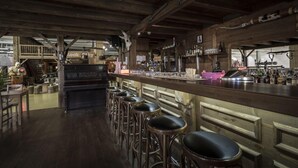 A rustic bar area with wooden beams, a bar counter, stools, and various bottles and glasses. - Mercure Chur City West (Chur)