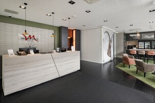 Zona de recepción de un hotel moderno con un mostrador de mármol, un bar con asientos y una gran obra de arte abstracta en la pared.