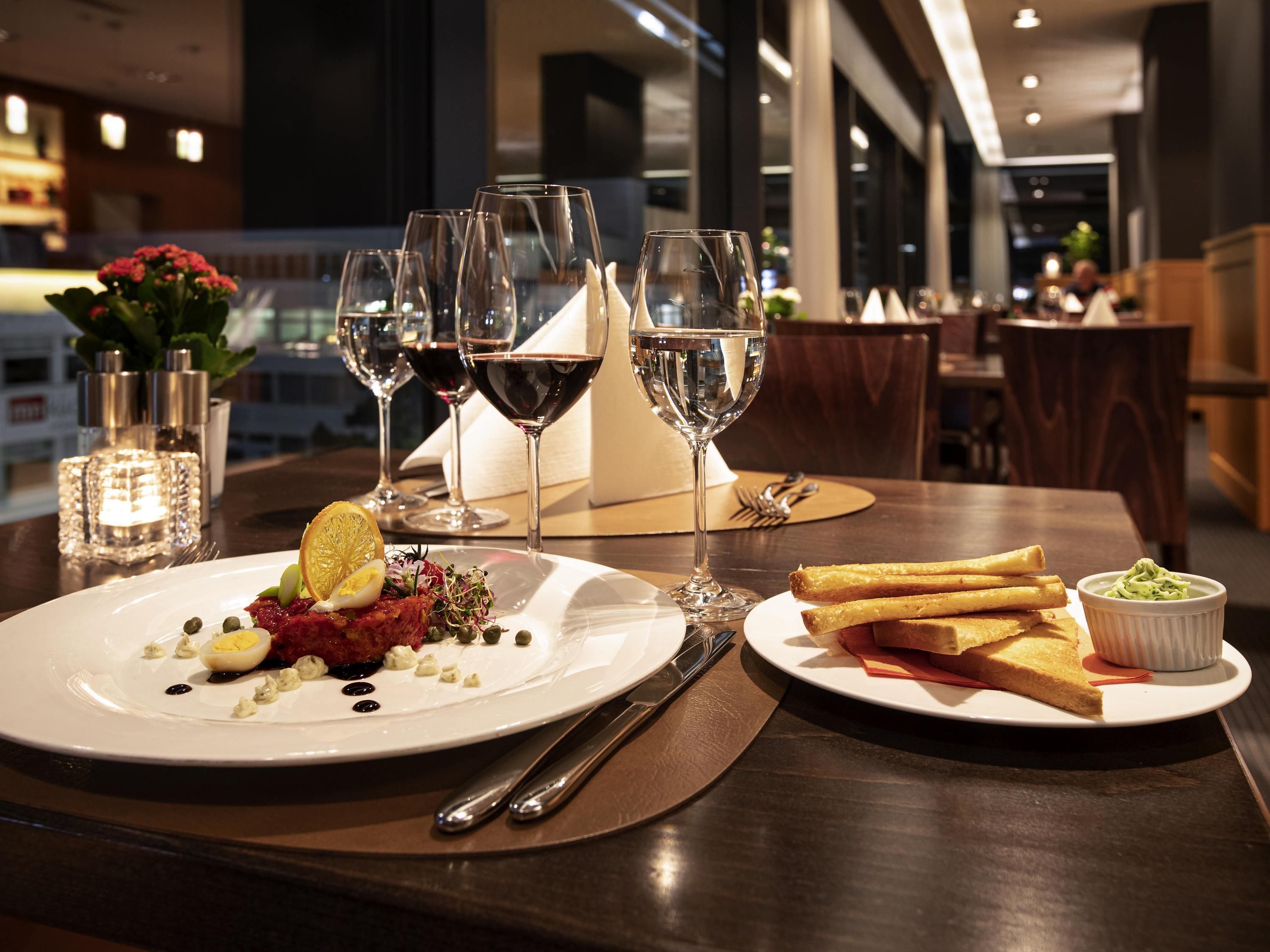 A dining table with plates of food, wine glasses, and cutlery.