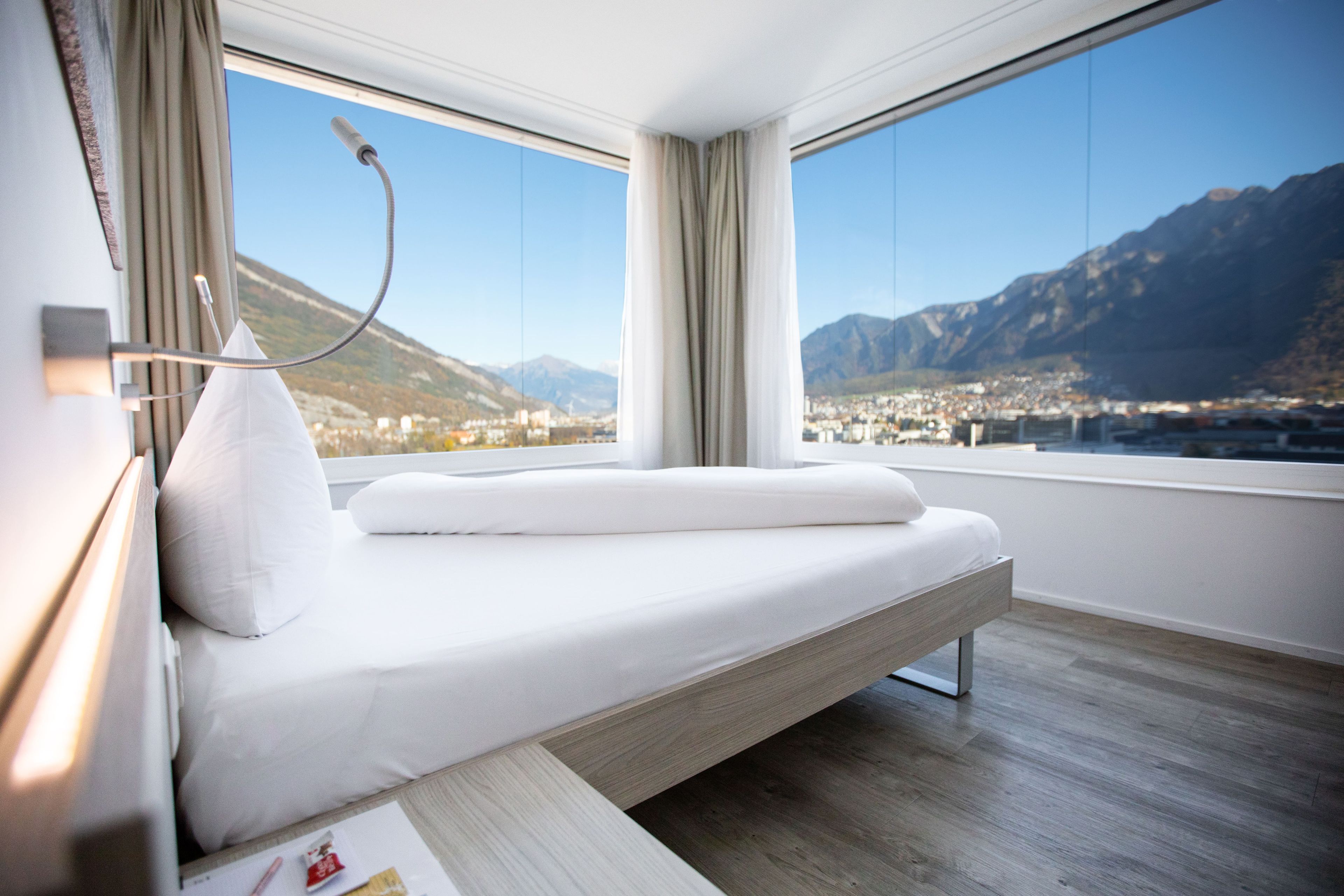 Ein modernes Zimmer mit einem Bett, einem Nachttisch und Blick auf eine Berglandschaft.