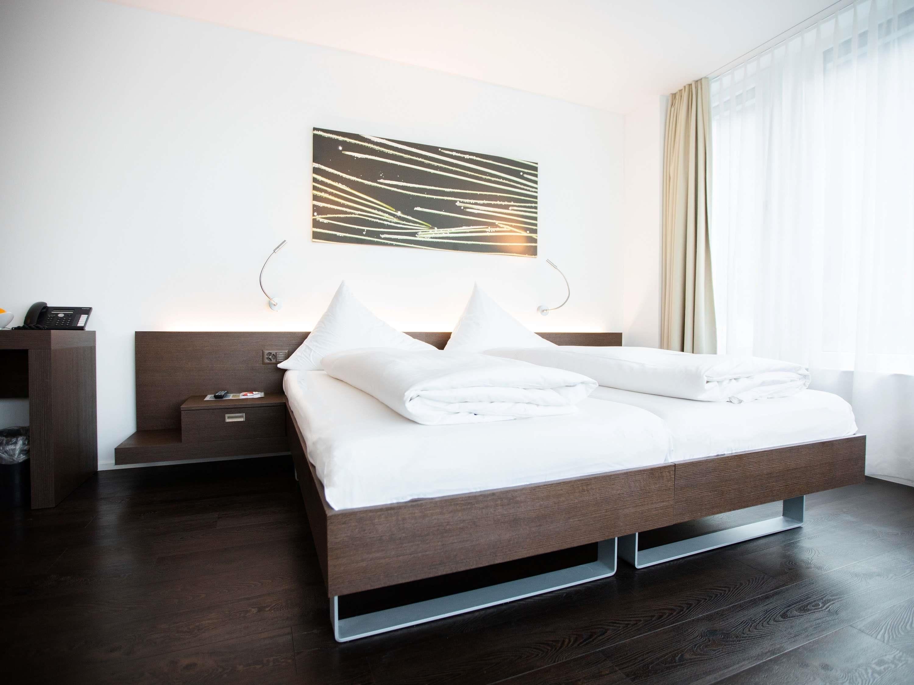 A modern hotel room with a large bed, bedside tables, a desk, and a wall-mounted artwork.