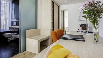 Ein modernes Zimmer mit Schreibtisch aus Holz, einem Stuhl, einem Laptop, einer Vase mit Blumen und Blick ins Badezimmer.