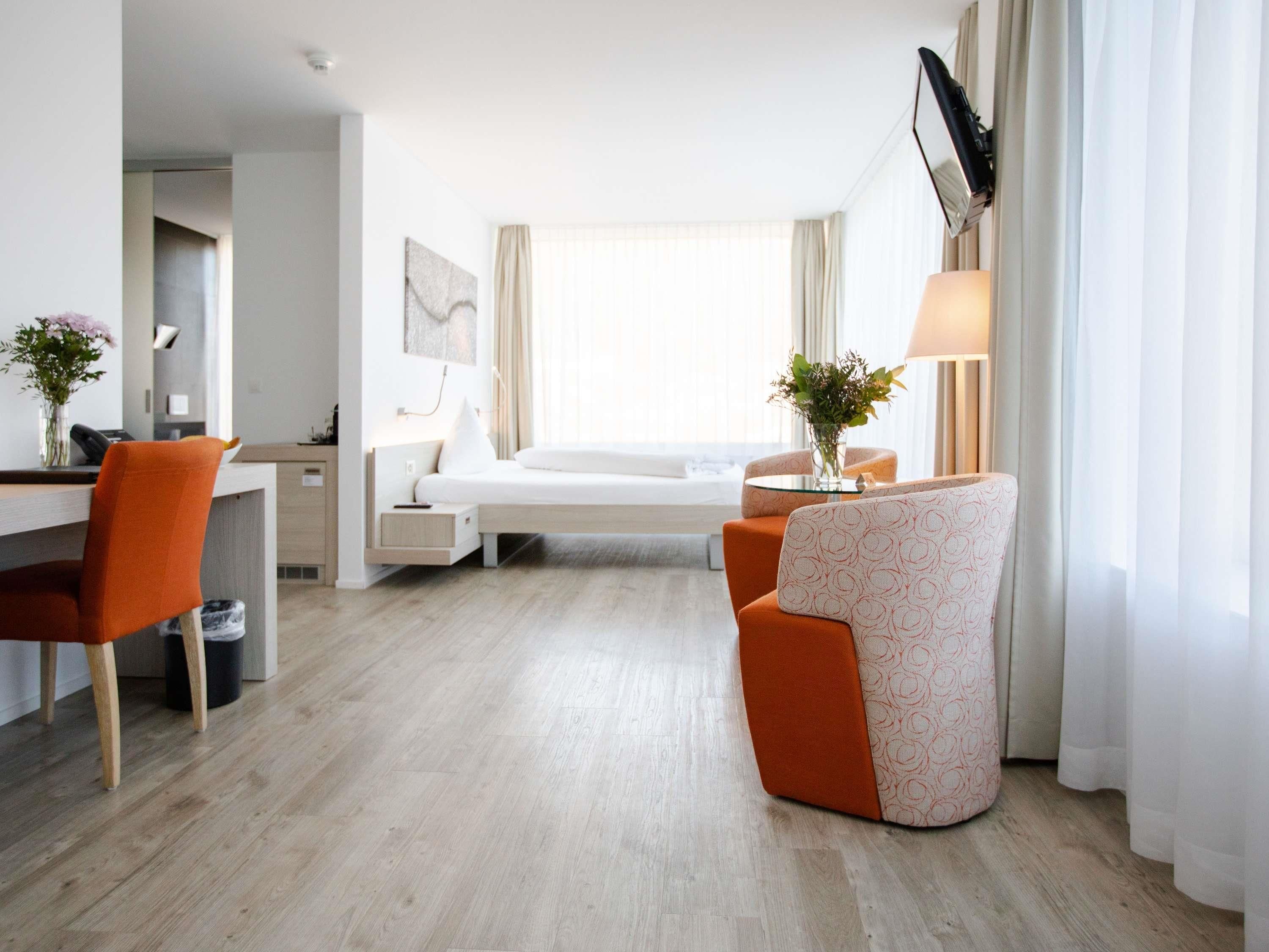 Ein Hotelzimmer mit Bett, Schreibtisch, Stuhl, Lampe und einer Vase mit Blumen.