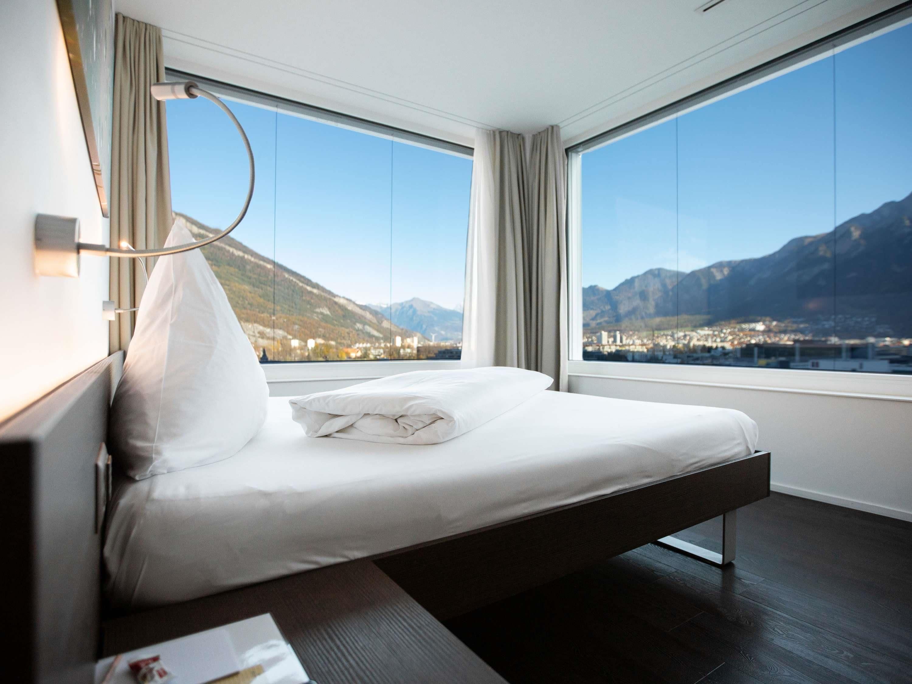 Une chambre d’hôtel moderne avec un lit, de grandes fenêtres et une vue sur les montagnes.