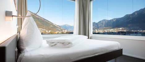 Une chambre d’hôtel moderne avec un lit, de grandes fenêtres et une vue sur les montagnes.
