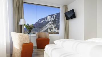 Habitació d'hotel amb un llit, dues butaques, un televisor, una finestra que dona a vistes de muntanya i una taula petita amb una planta.