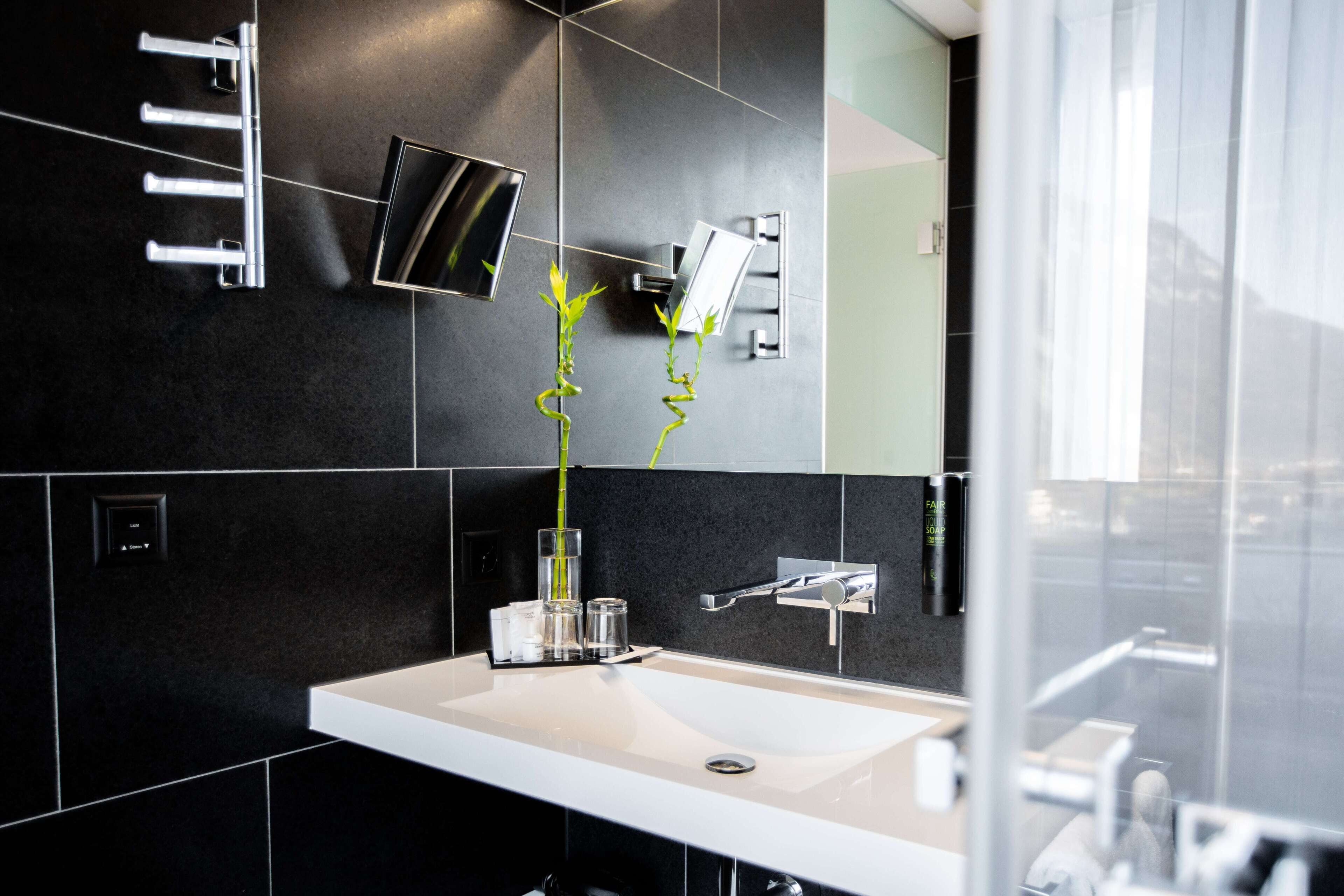 A modern bathroom with a white sink, black tiles, a glass shower enclosure, and a mirror.