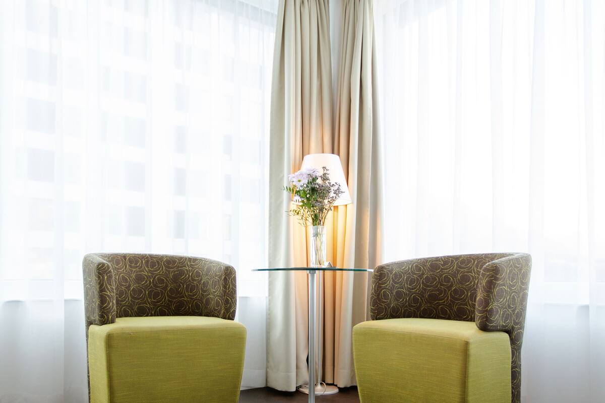 A room with two green armchairs, a floor lamp, and sheer curtains.