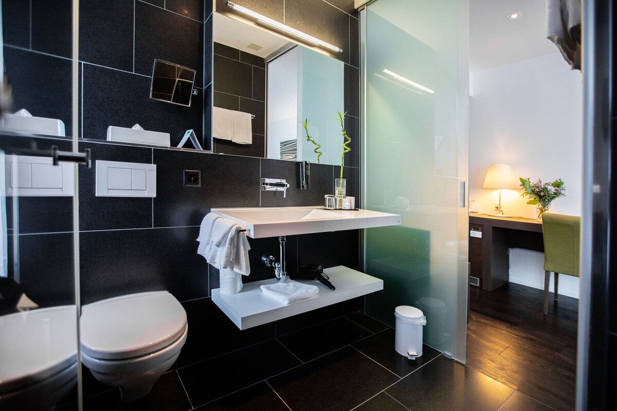 A modern bathroom with a white sink, dark tiles, a mirror, and a toilet.