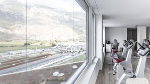 A gym with exercise equipment and a large window overlooking a mountainous landscape. - Mercure Chur City West (Chur)