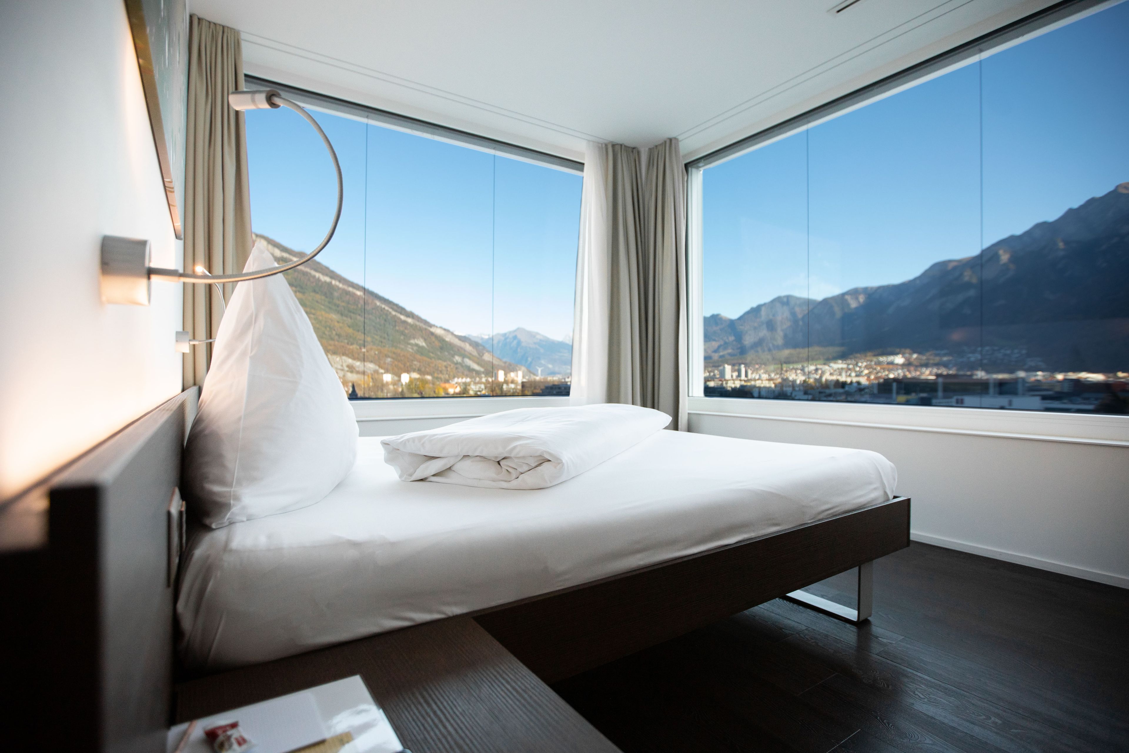 A hotel room with a bed, a view of mountains, and a cityscape.