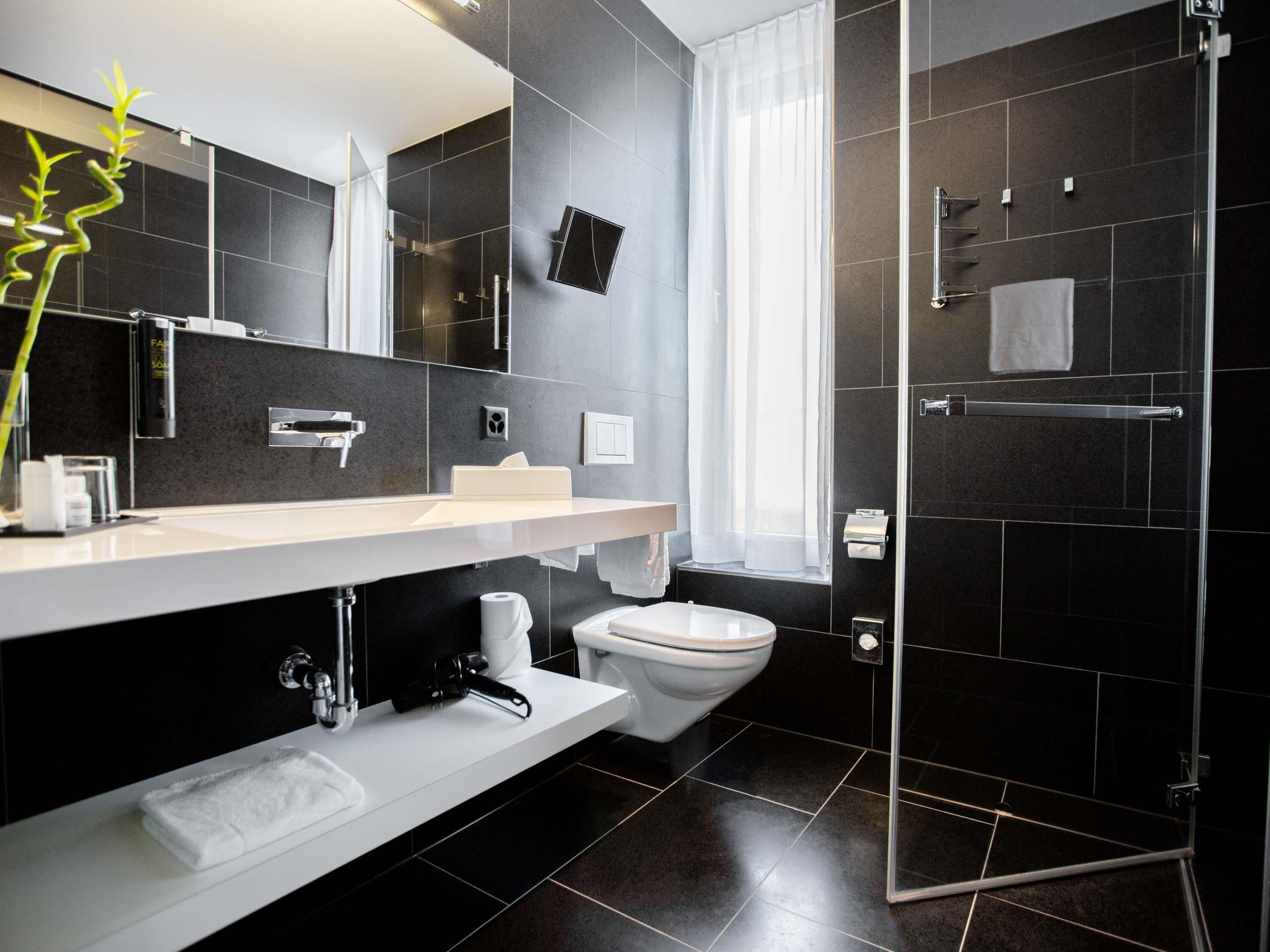 Un baño moderno con un espejo grande, lavamanos blanco y cabina de ducha de vidrio.