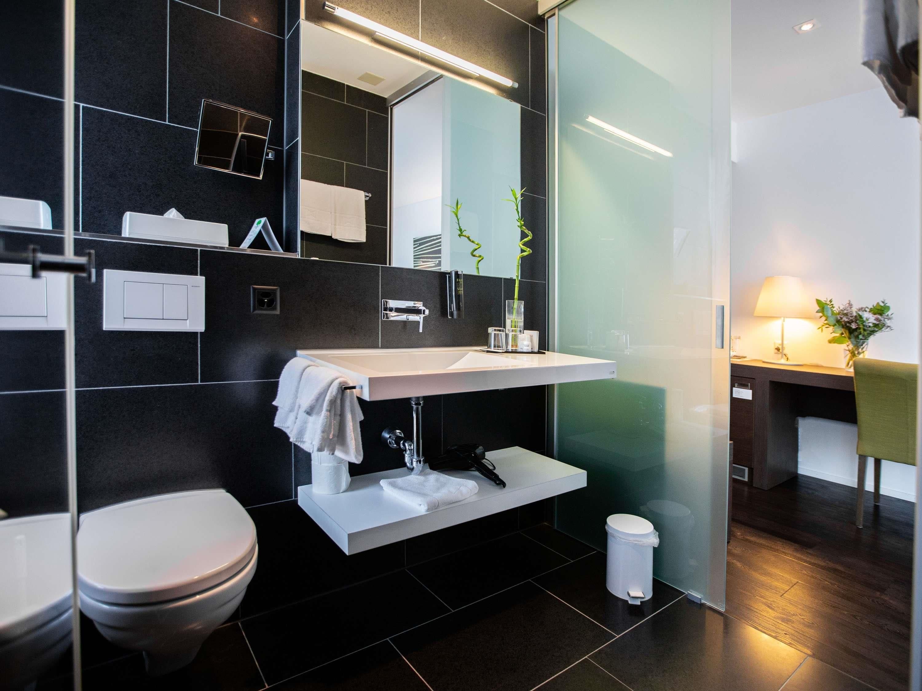 Ein modernes Badezimmer mit einem weißen Waschbecken, einer Toilette und einem Spiegel.