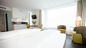 A hotel room with a large bed, a desk with a chair, a small table with a vase, and a TV on the wall.