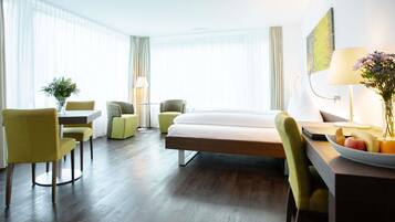 Habitación de hotel con cama, dos sillas, una mesa y un escritorio con frutero.