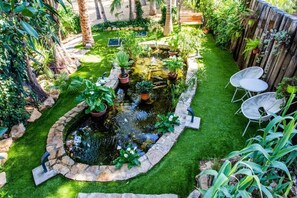 A garden with a pond, green lawn, and two white metal chairs. - El Palmeral de Madaria (Alicante)