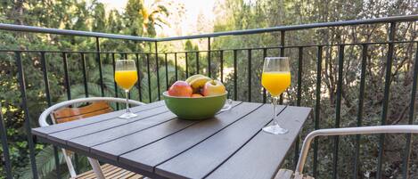 A balcony with a wooden table, a green bowl with fruits, and two glasses of orange juice.