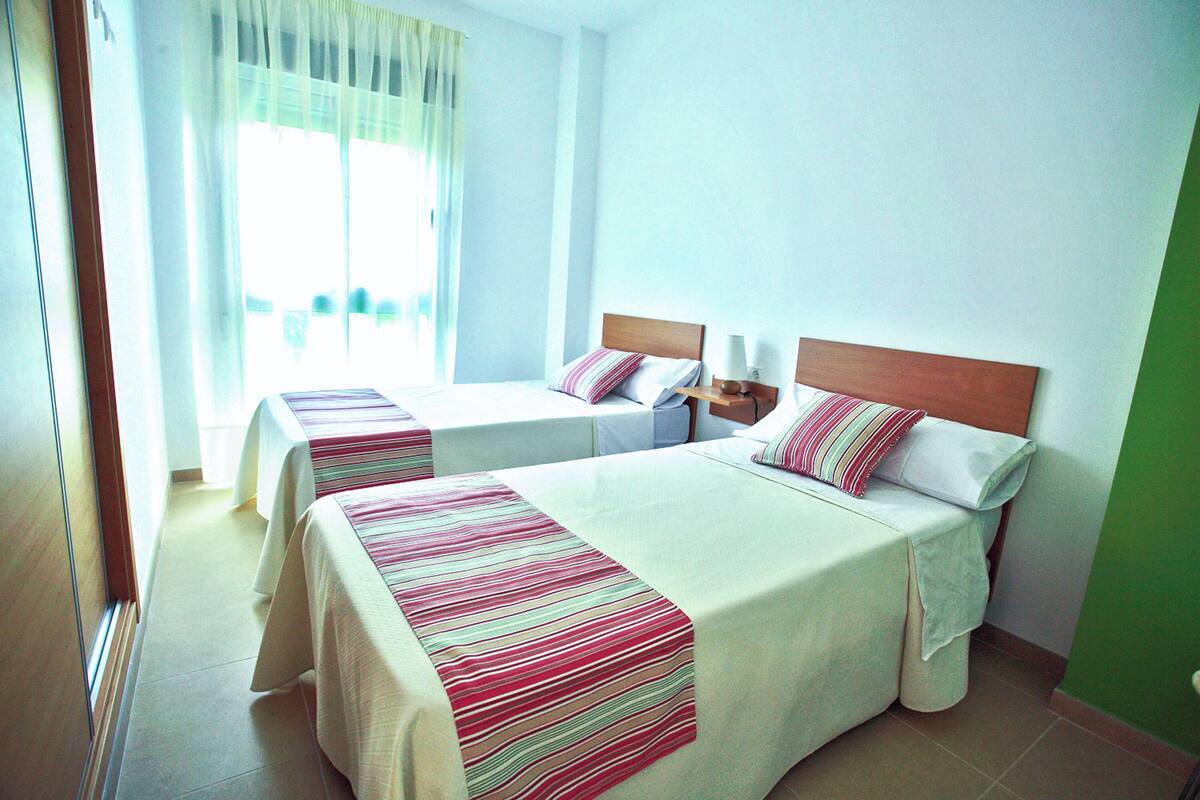 Ein Hotelzimmer mit zwei Betten, jeweils mit einem Holz-Kopfteil, weißer Bettwäsche und gestreifter Decke.