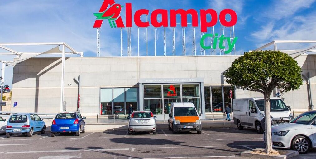 Un parking où sont garées plusieurs voitures et un bâtiment sur lequel on peut lire l’inscription « Alcampo City ».