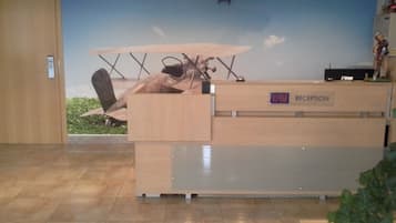 A reception desk with a wooden finish, a clock on the wall, and a small statue on top.