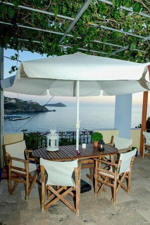 A wooden table with a white canopy, surrounded by chairs, overlooking a coastal view. - Melina's sunset (Kalymnos)