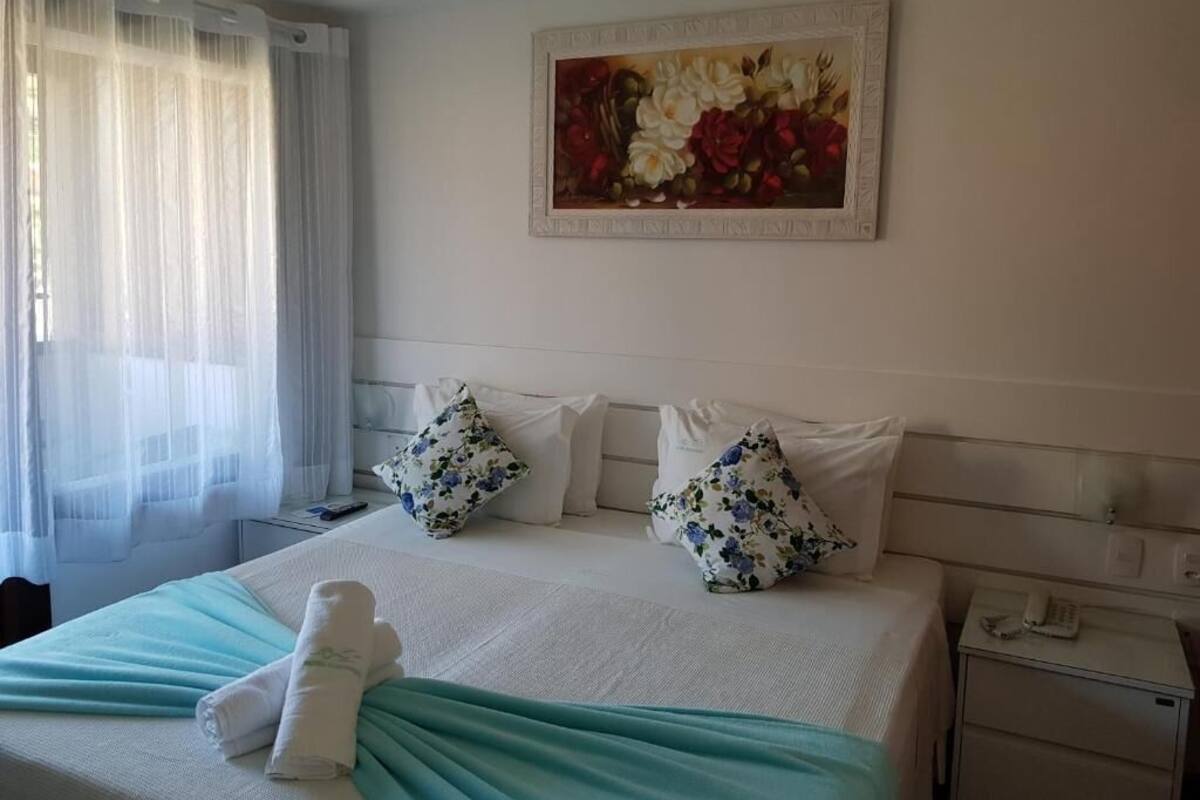 Une chambre d’hôtel avec un lit, un tableau, une table de chevet et une fenêtre avec des rideaux.