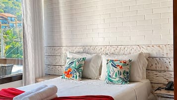 Habitación de hotel con cama, mesita de noche, pared de ladrillo blanco y ventana con cortinas.