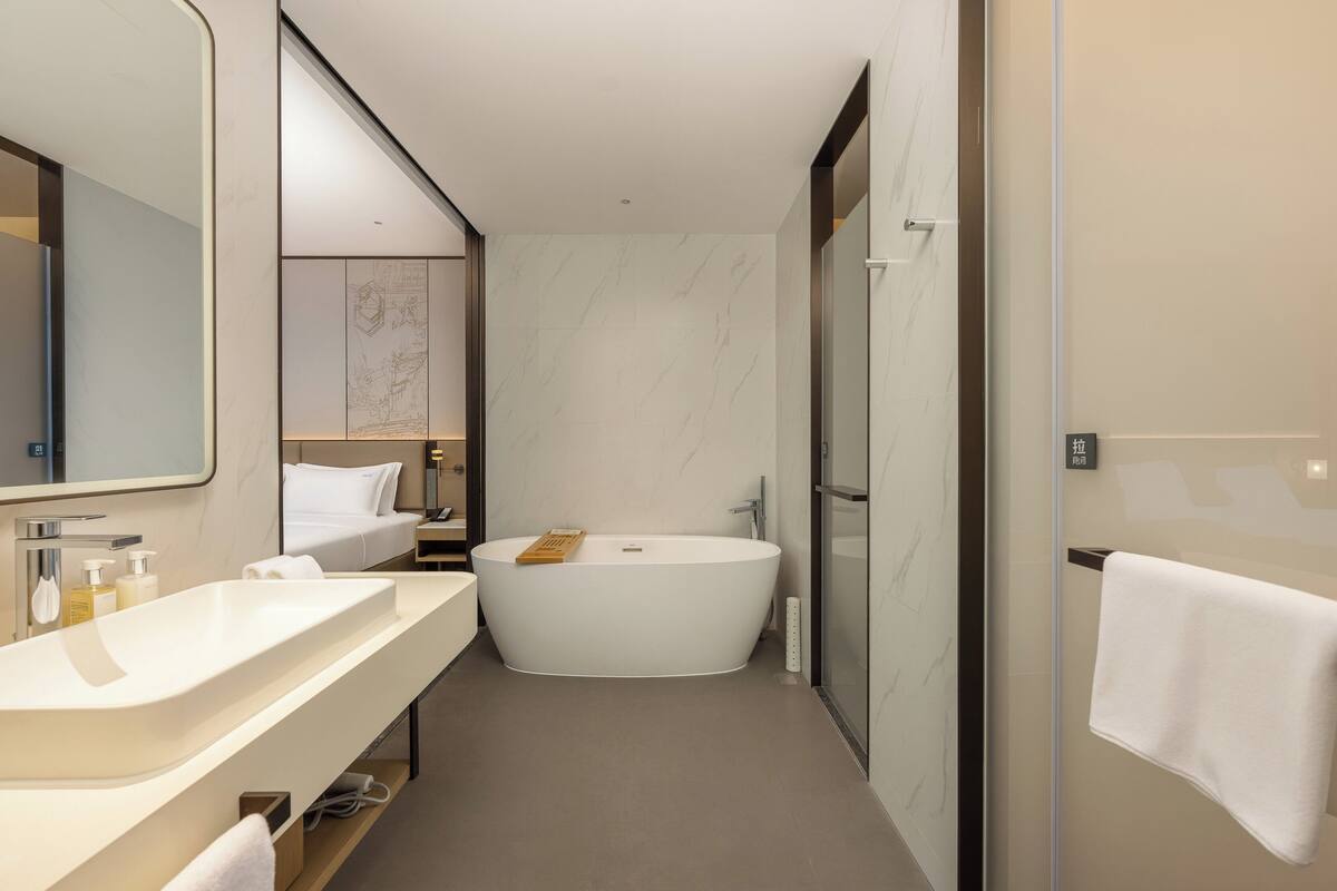 Un baño moderno con una bañera independiente, un espejo grande y un tocador con lavamanos y encimera.