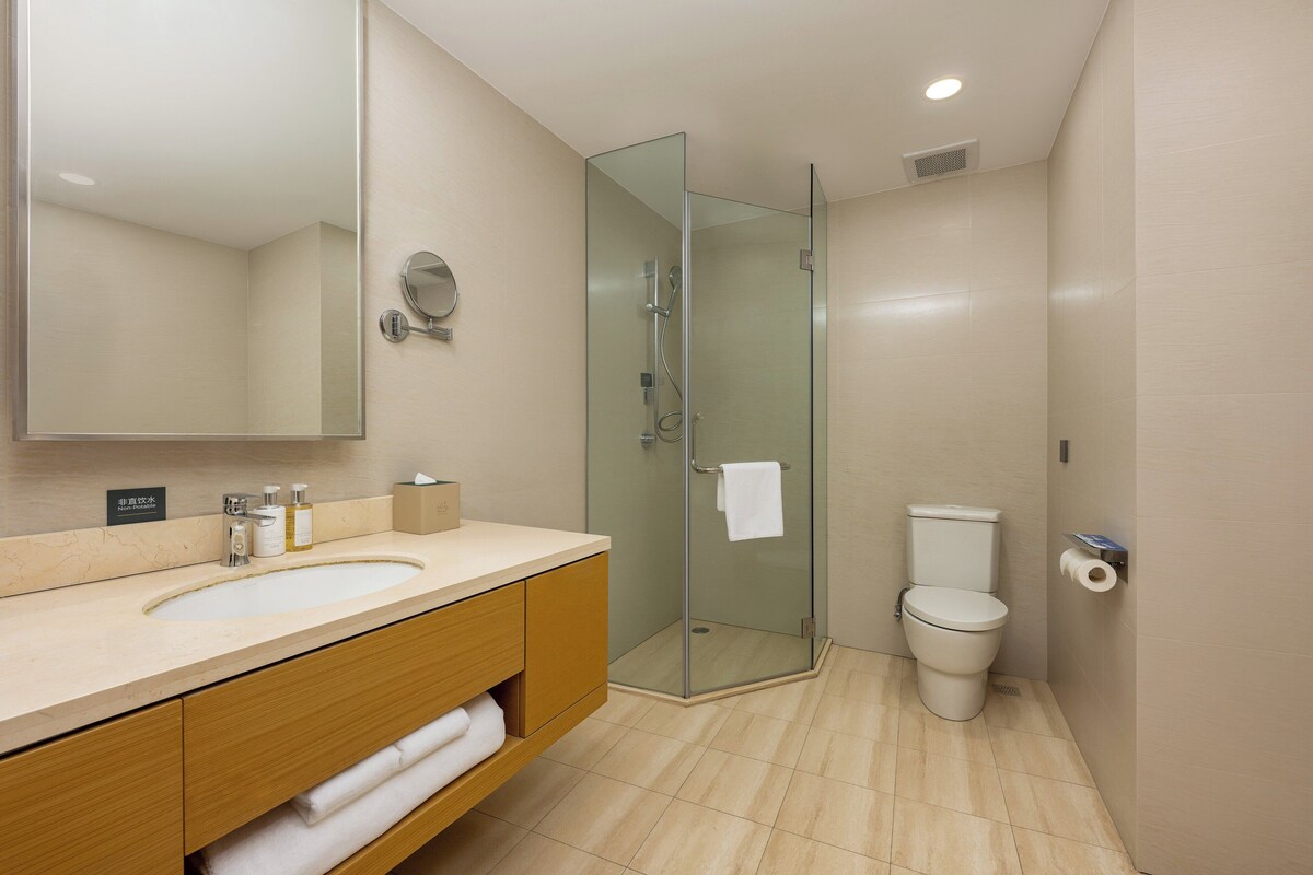 Un baño moderno con ducha envuelta en vidrio, inodoro y lavamanos con espejo.