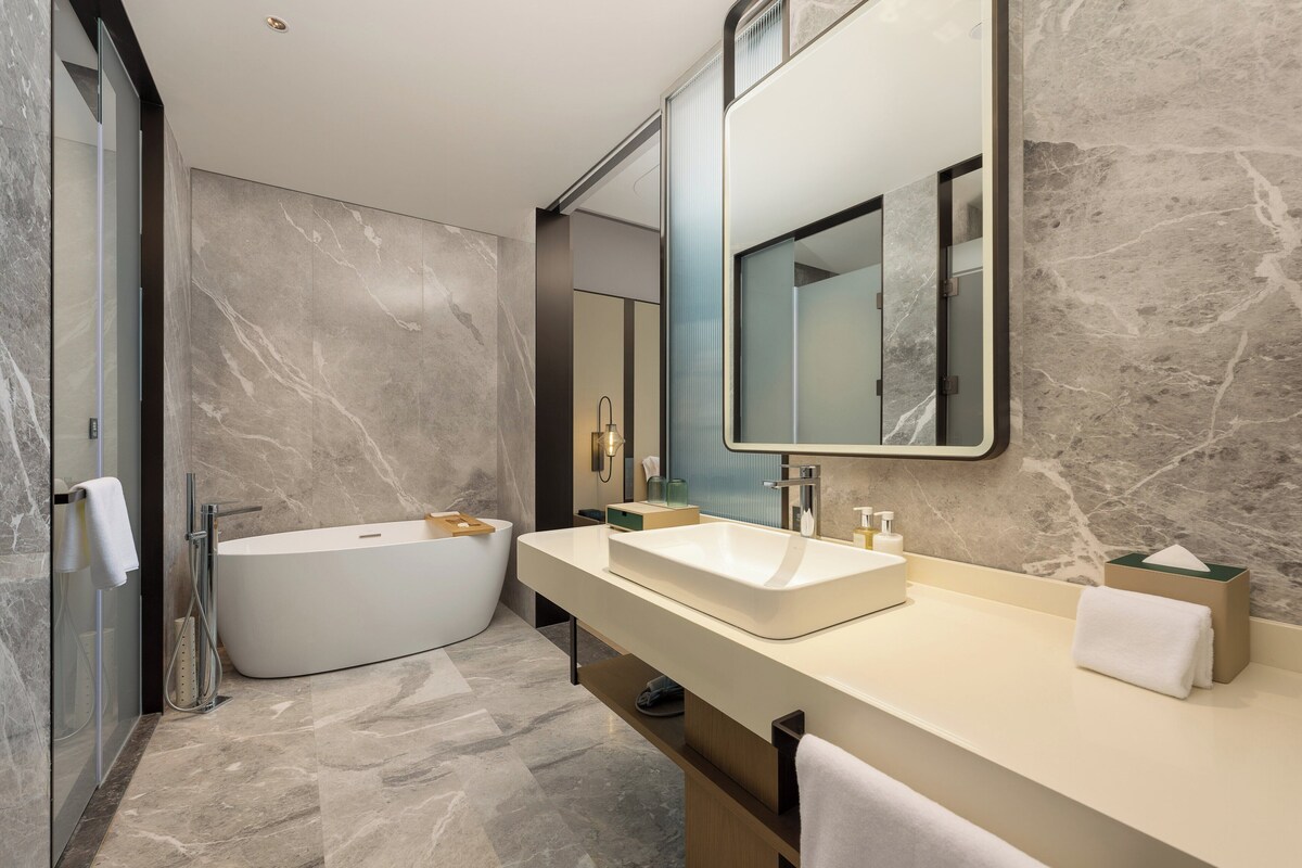 Un baño moderno con una bañera independiente, un mueble de tocador amplio con espejo y paredes de mármol.