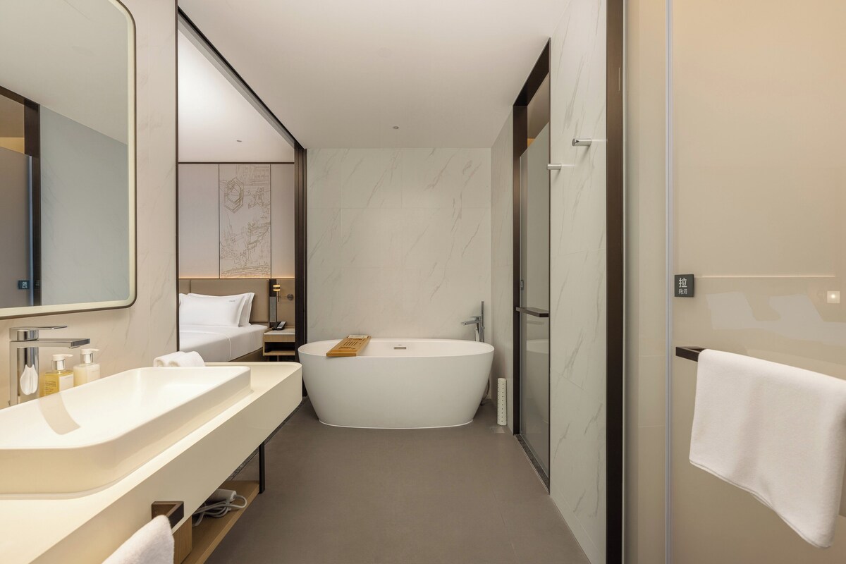 Un baño moderno con una bañera independiente, un espejo grande y un tocador con lavamanos y encimera.