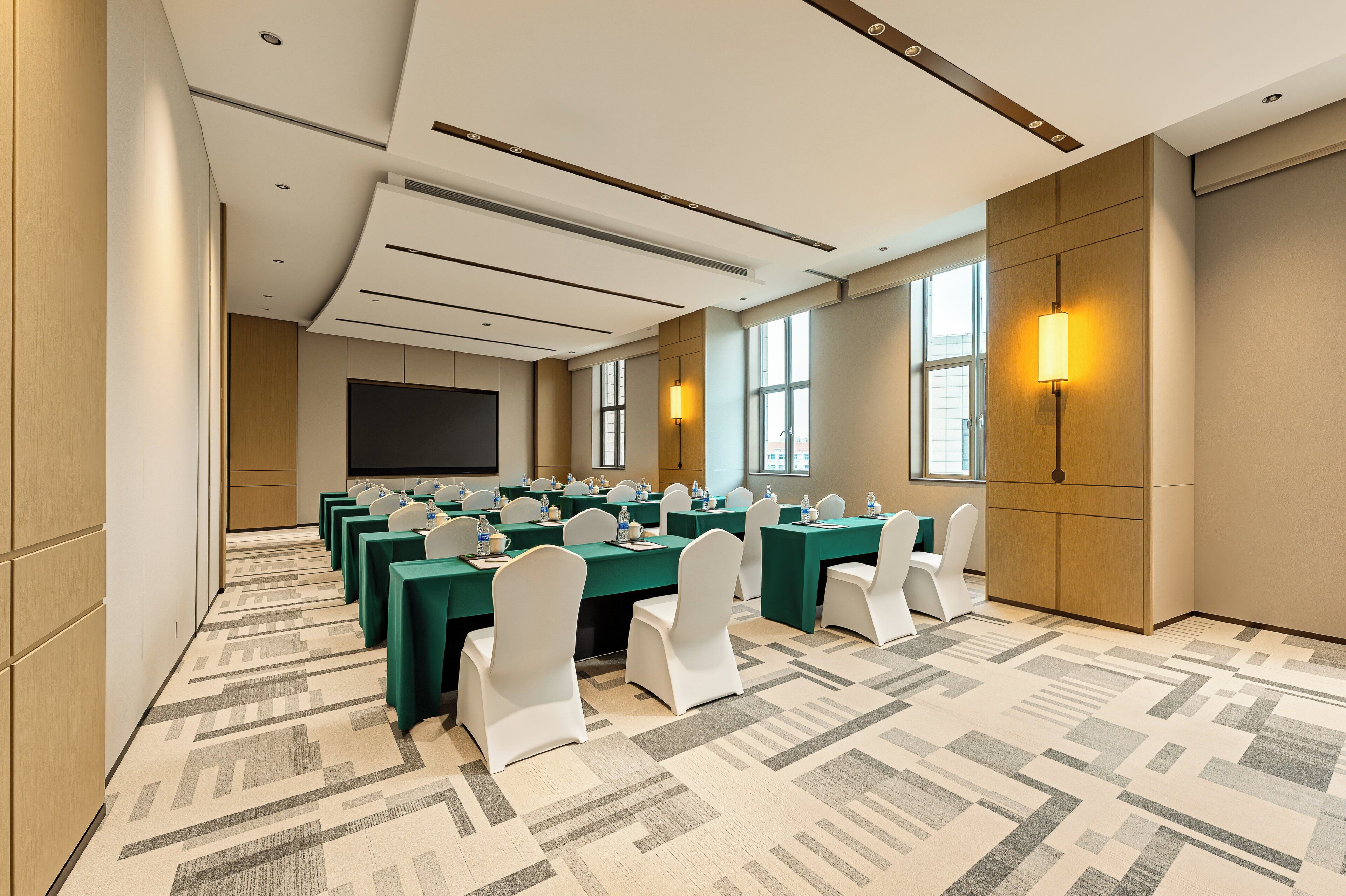 A conference room with multiple tables, white chairs, and a large screen.