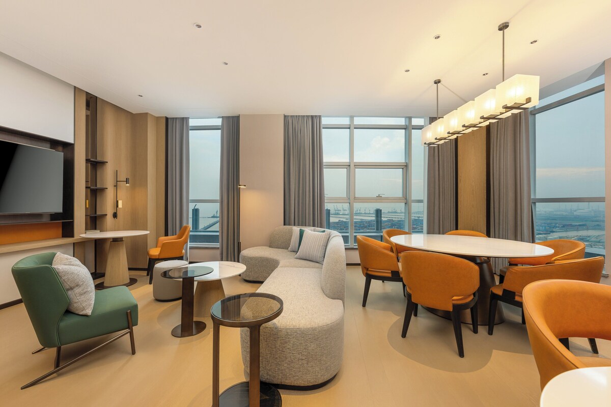 Una habitación de hotel moderna con un ventanal grande, un sofá, una mesa de comedor y un televisor.