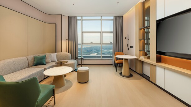 Une chambre d’hôtel moderne équipée d’un canapé, d’un pouf, d’une table ronde et d’un téléviseur posé sur un meuble.