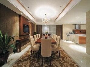 Un comedor moderno con una mesa y sillas de madera, una araña y una cocina al fondo.