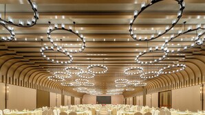 Une salle de banquet dotée de nombreuses tables rondes, de chaises blanches et d’un plafond au design moderne.