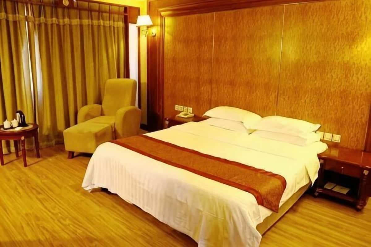 Een hotelkamer met een groot bed, een stoel, een nachtkastje en een lamp.