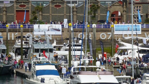 A marina with multiple yachts docked, a building with a classical facade, and a crowd of people. - Liberty Wharf Apartments (St. Helier)