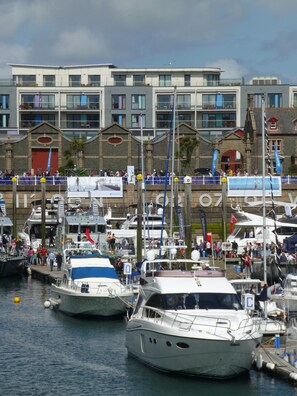 A marina with multiple yachts docked, a building with a classical facade, and a crowd of people. - Liberty Wharf Apartments (St. Helier)