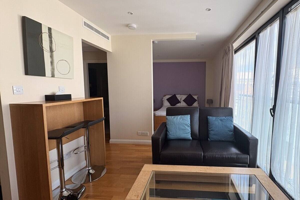 A modern living room with a black leather sofa, a glass coffee table, and a wooden console table.